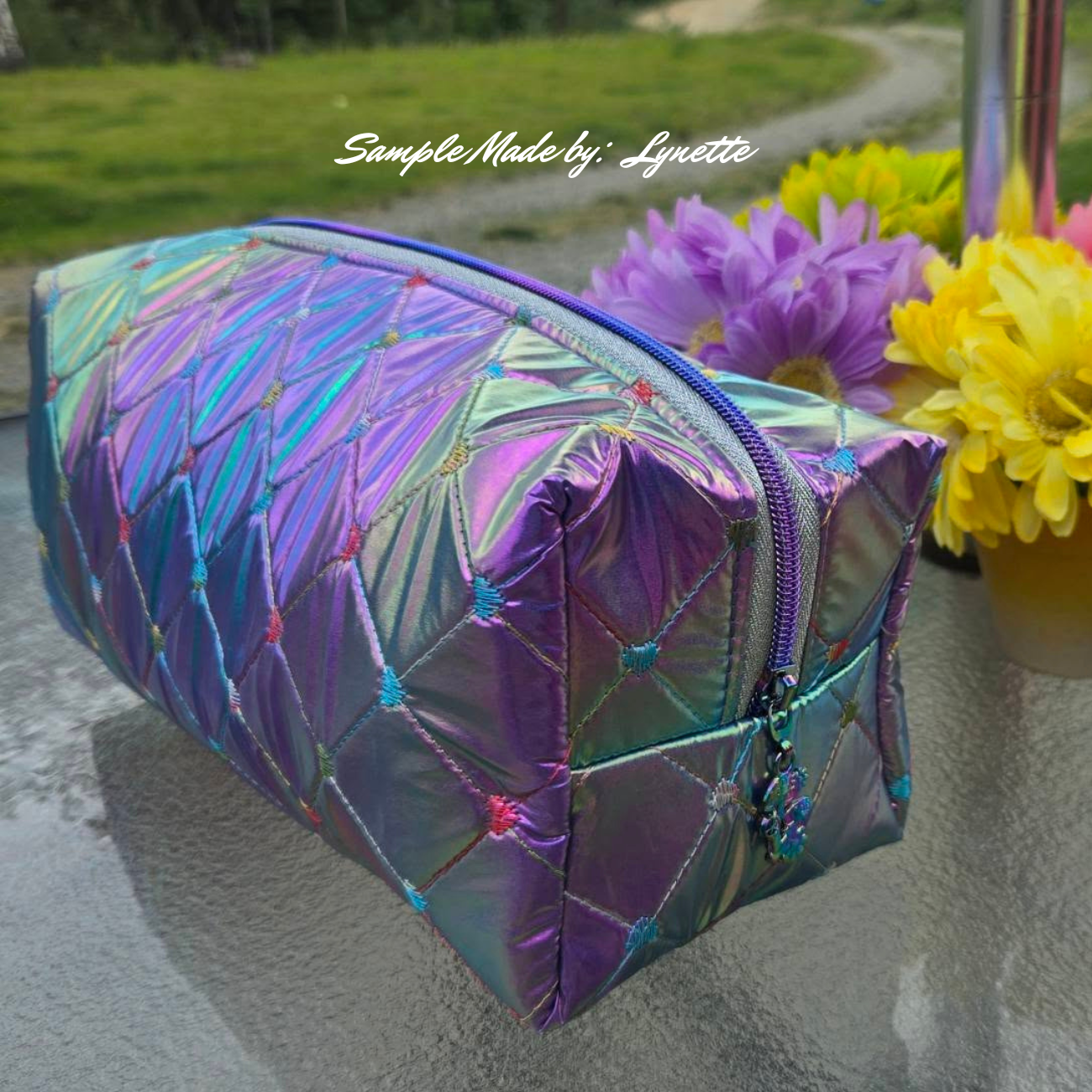 Iridescent makeup bag with geometric pattern on a stone surface with flowers in the background