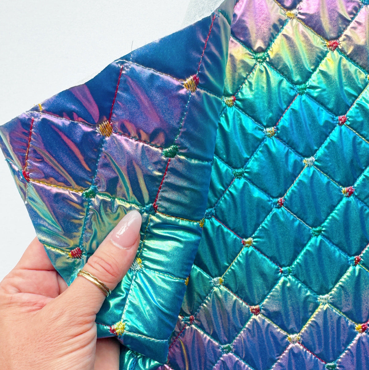 Multicolored quilted fabric held by a hand with a white background